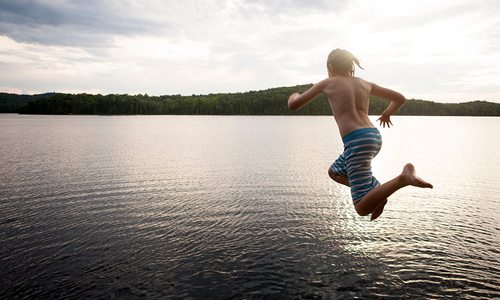 Boy in swim trunks in mid-air jumping into beautiful cove water