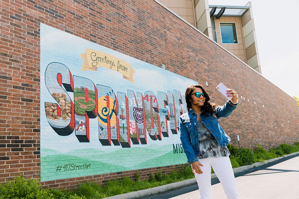 Young girl takes a selfie on a beautiful sunny summer day in front of mural in downtown Springfield, MO