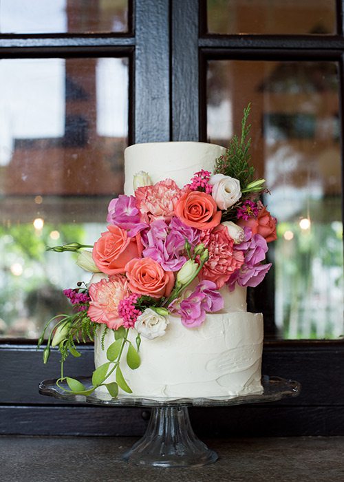 All white wedding cake with bold colored flowers