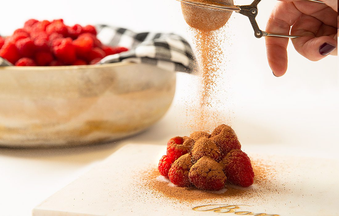 Sprinkling Askinosie Chocolate Cocoa Powder on raspberries