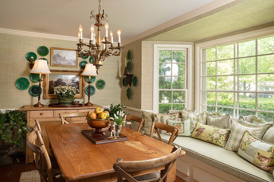 dining room with sage green pillows on window seat and fruit bowl on table with antiques