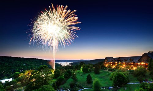 Fireworks lighting up the night sky above a hillside lodge overlooking Table Rock Lake.