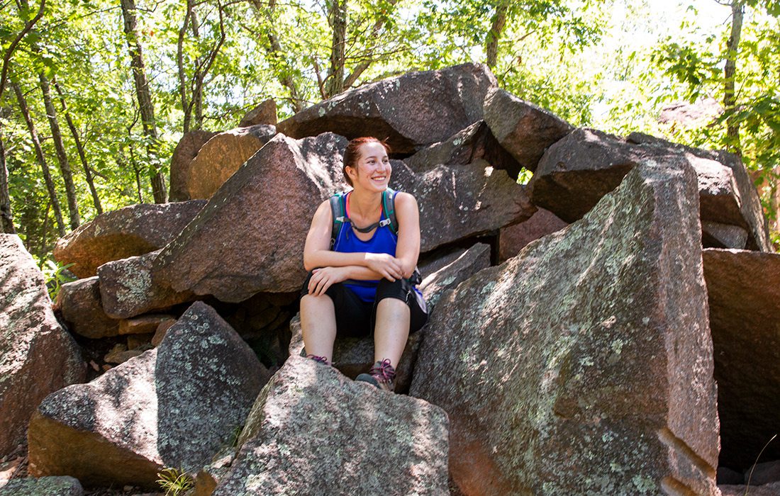 the author sits on a collection of rocks in a wooded area