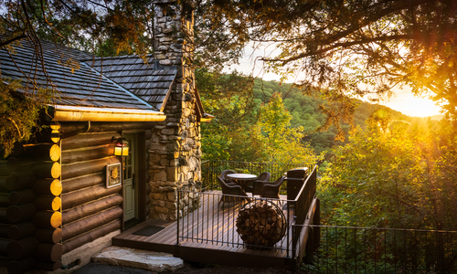 A rustic log cabin and private deck overlook the wooded Ozark hills at Big Cedar Lodge during golden hour.