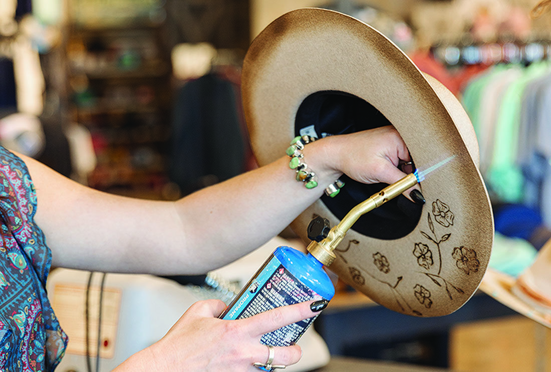 A woman holds up a hat and blowtorches the edge.