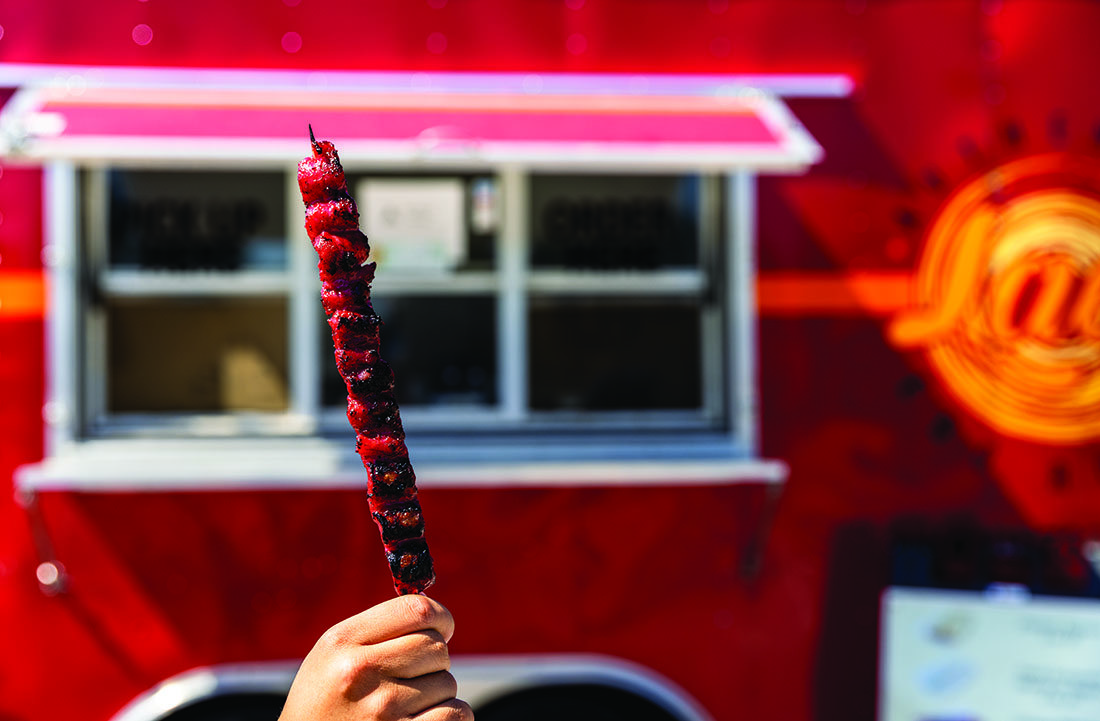 A pork skewer held aloft in front of the food truck.