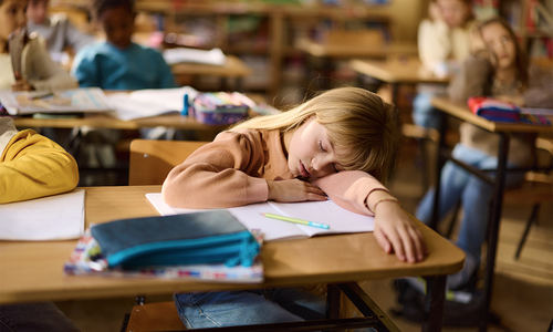 Child falling asleep at their desk in school.