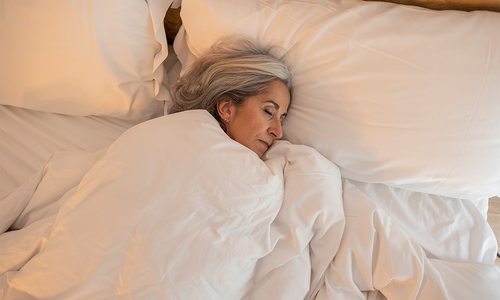 Woman peacefully sleeping in a bed with soft white bedding in a calm, restful setting.