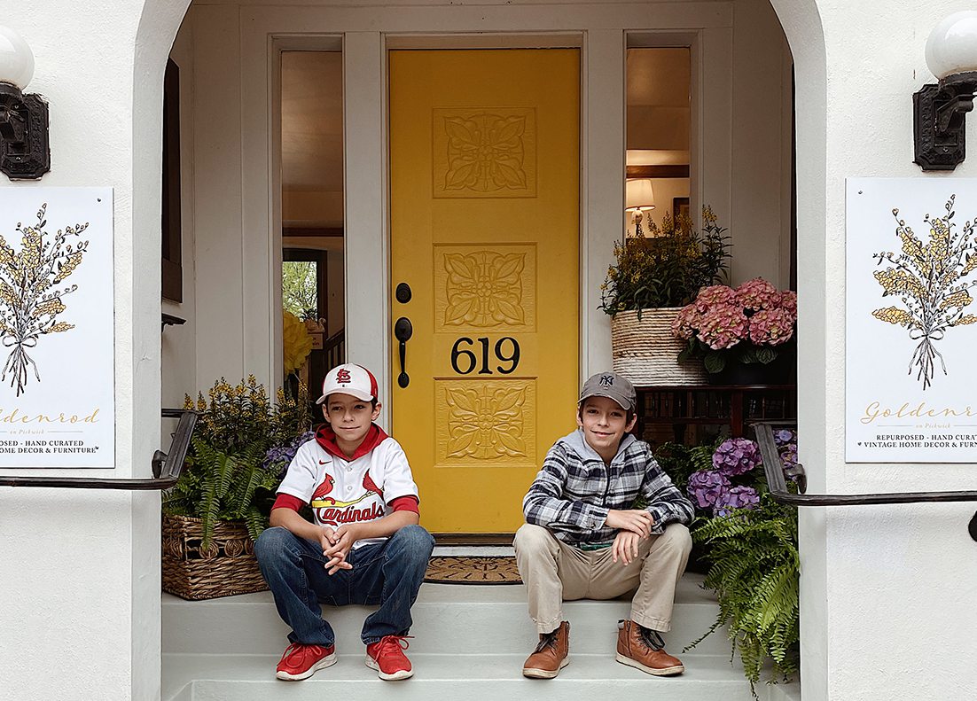 two boys sit outside local shop with yellow door