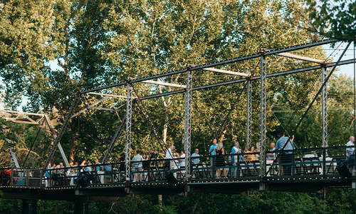 Guests gather around dining tables during an outdoor event on the historic Finley Farms bridge.