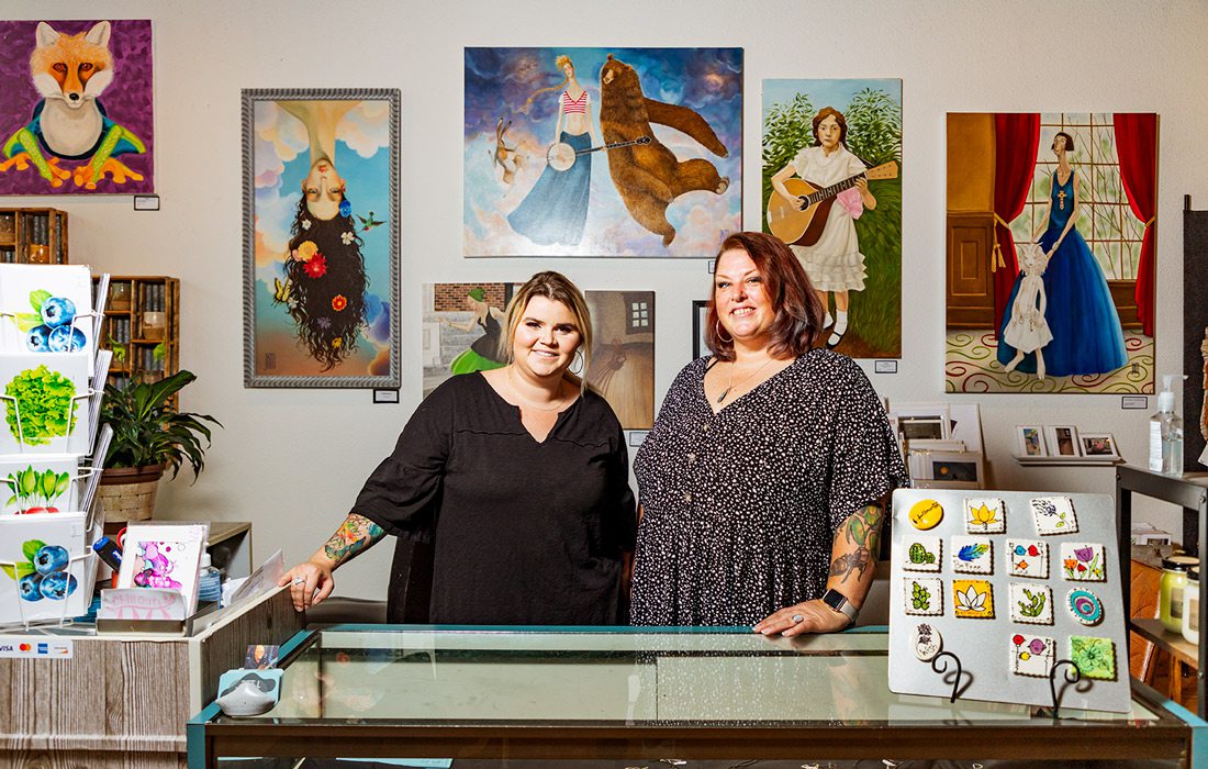 Two women in front of counter at art gallery.