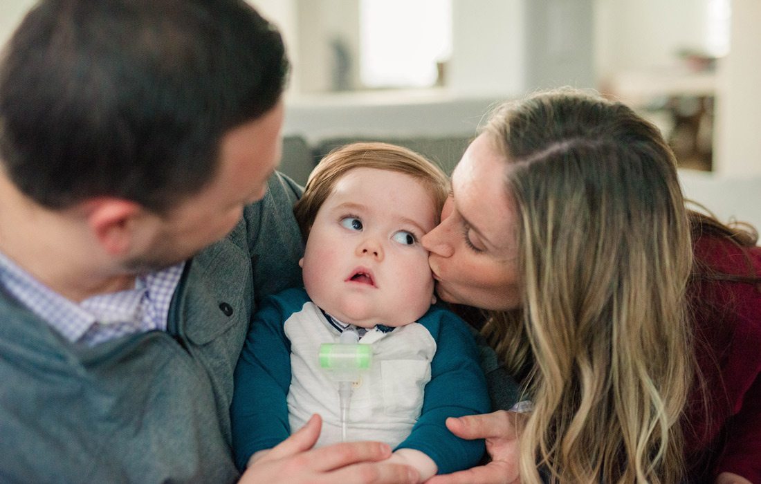 Parents hold baby and mom kisses babies cheek