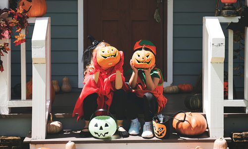 Two little kids in Halloween costumes showing off their carved pumpkins