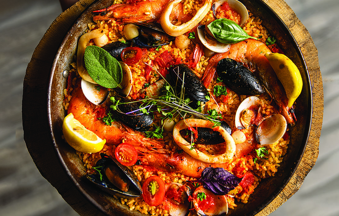 A plate of Paella Valenciana, a dish with red rice, seafood, and veggies.