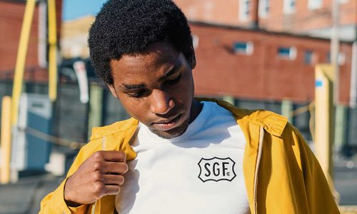 A man wears a yellow jacket and a white t-shirt with the letters "SGF" on it