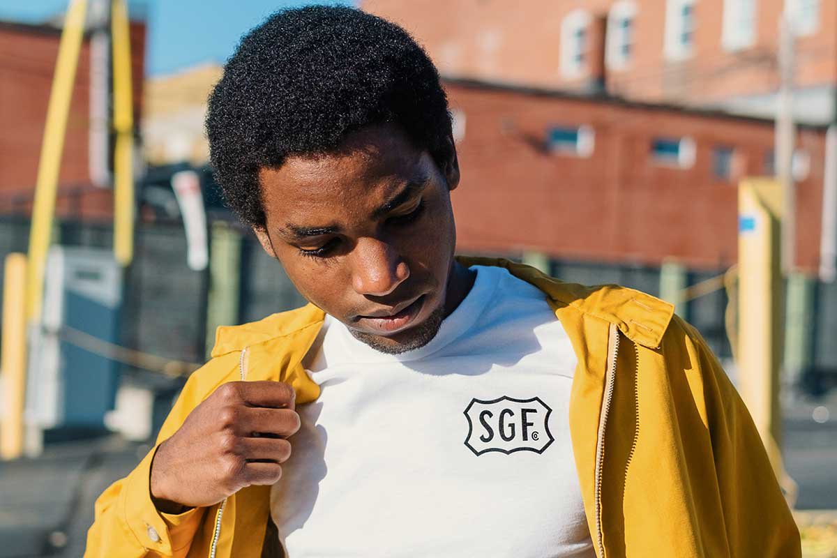 A man wears a yellow jacket and a white t-shirt with the letters "SGF" on it