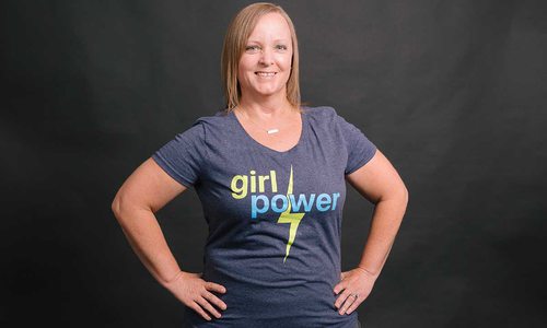 Shana stands with her hands on her hips, smiling in her "girl power" t-shirt