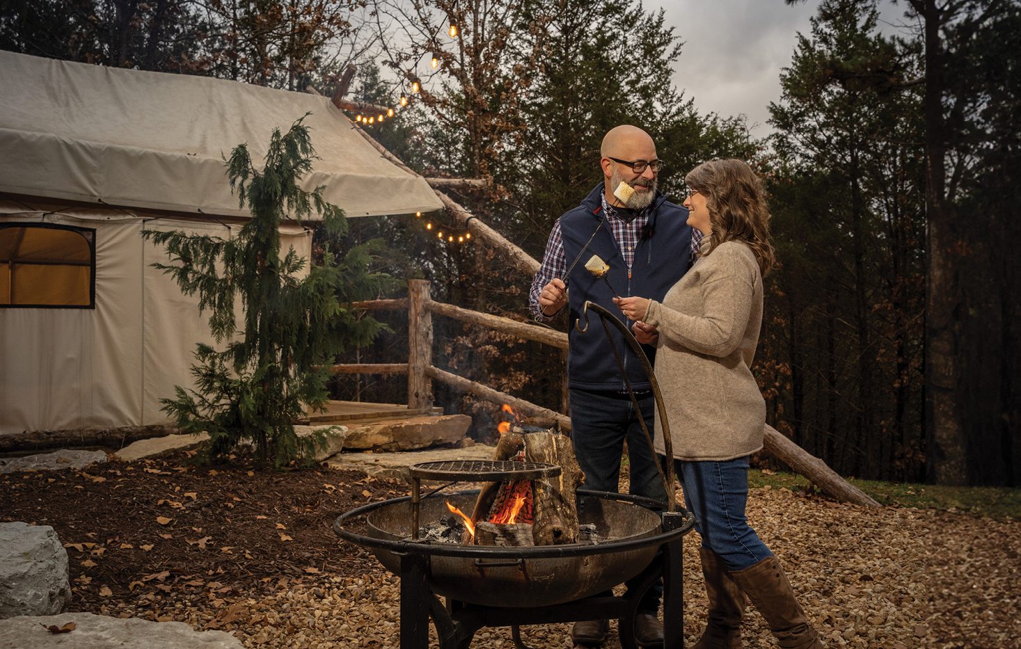 An older couple outside a luxury yurt standing around a fire