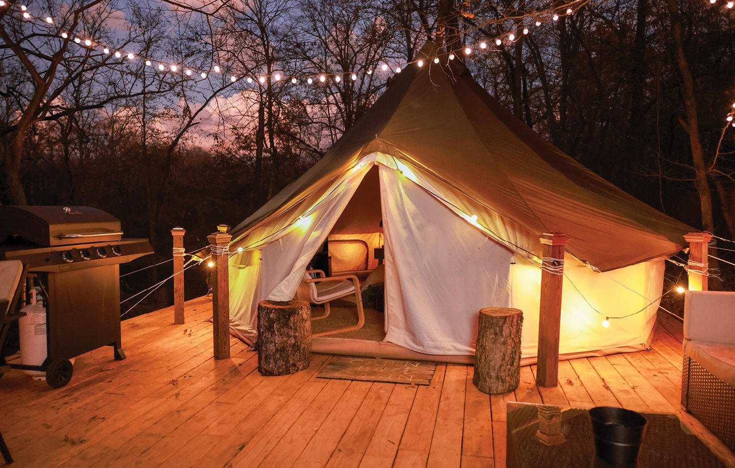 An outdoor glamping yurt on a wooden deck surrounded by fairy lights in the evening