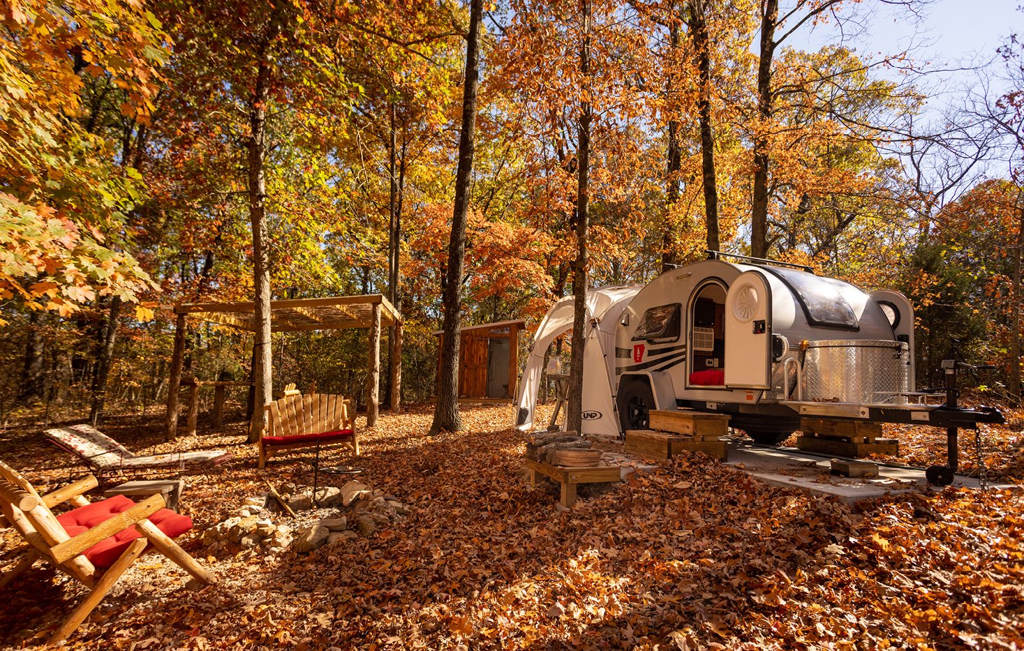 A silver airstream camper in a forest in the fall, surrounded by rich brown and orange leaves