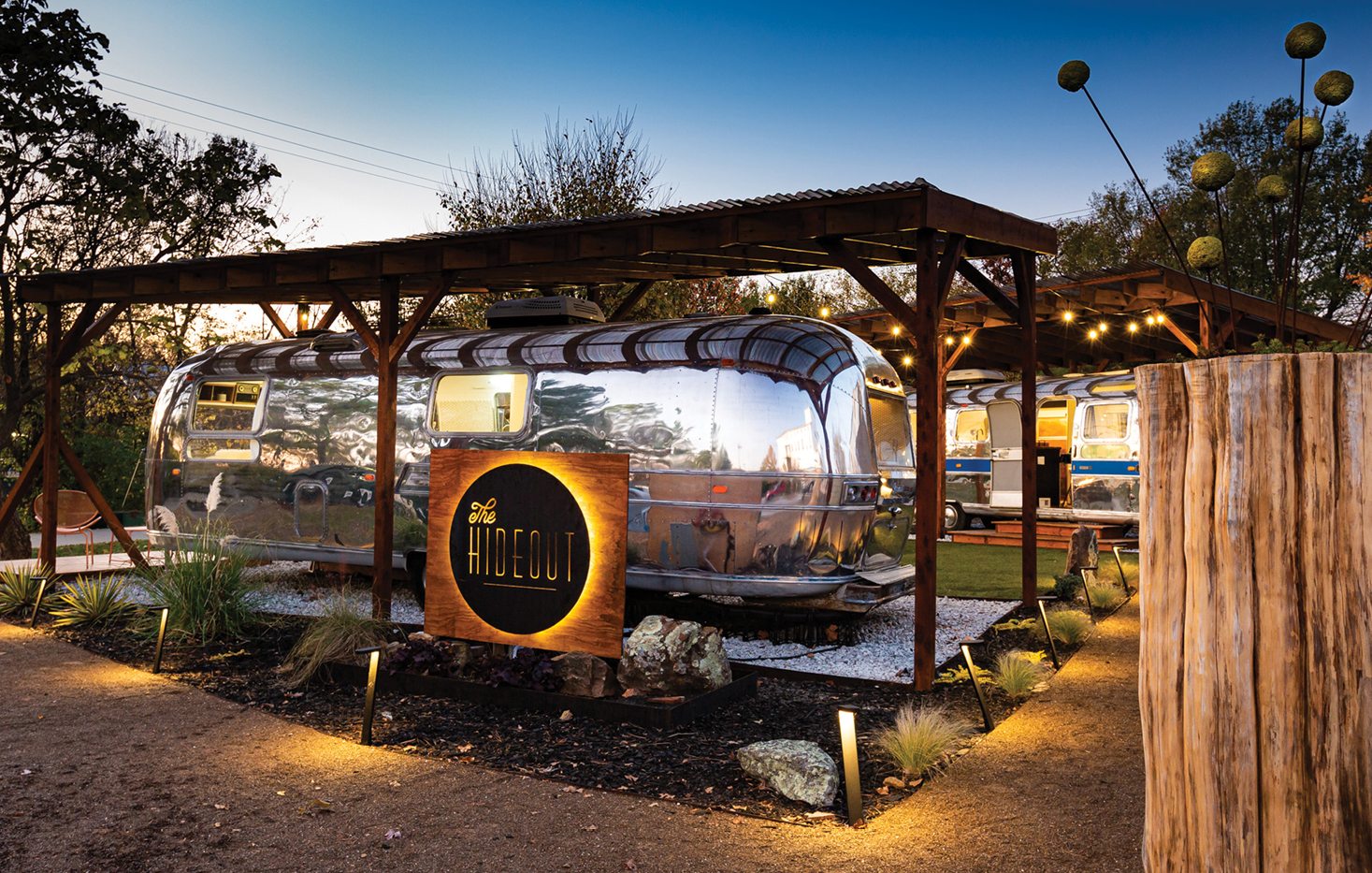 A luxury silver camper on a lot surrounded by decking and a cozy firepit