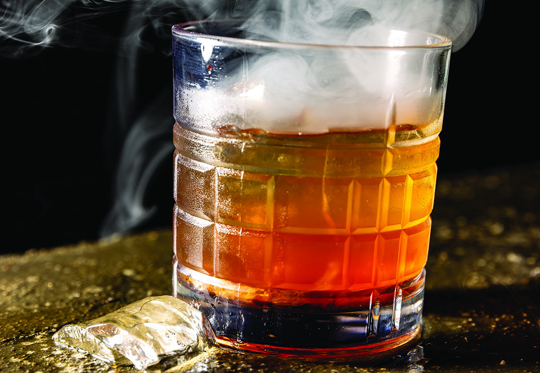 A smoking amber-colored cocktail in a glass.