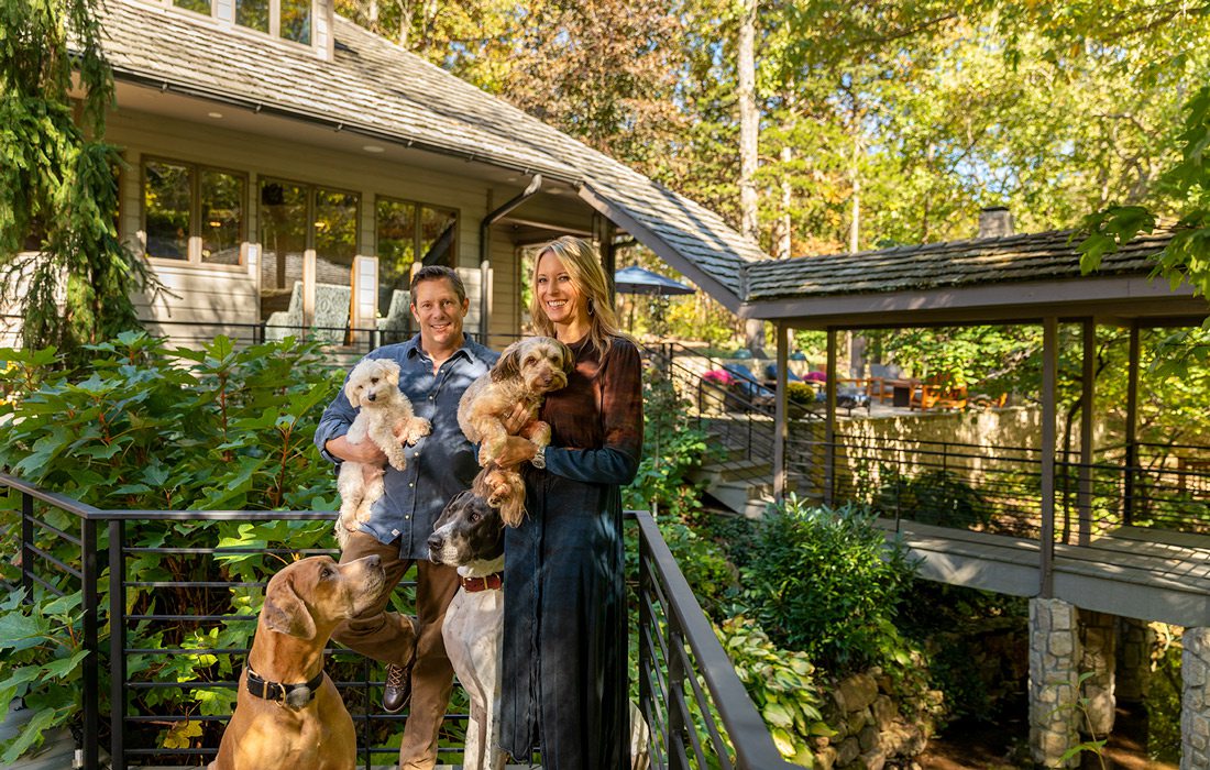 Man and woman pose with their three dogs in front of rustic modern home
