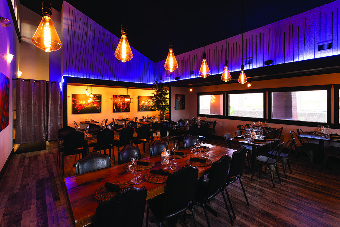The dining room at 65 Tapas, with dim lights, dark wood floors, and furniture in a contemporary style.