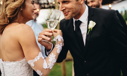 A bride and groom link arms in a champagne toast.
