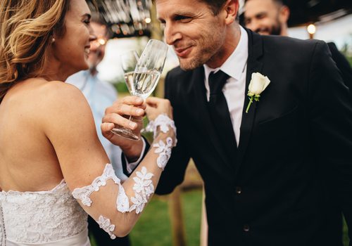 A bride and groom link arms in a champagne toast.