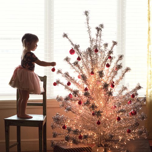 little girl adds ornaments to a Christmas tree