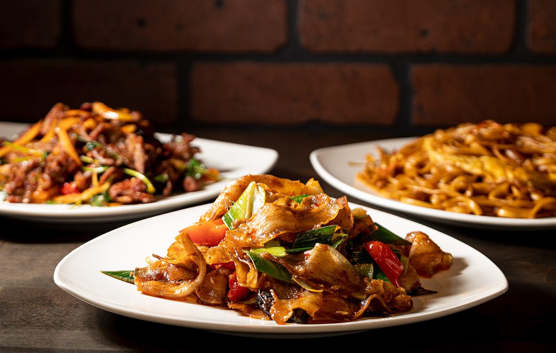 Three white plates of chinese food on wooden table