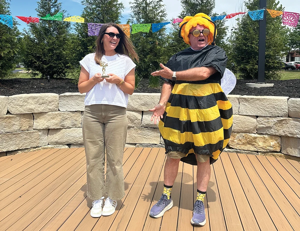 Tamra Lovelace holds a trophy beside Larry Hicks, who wears a bumblebee costume