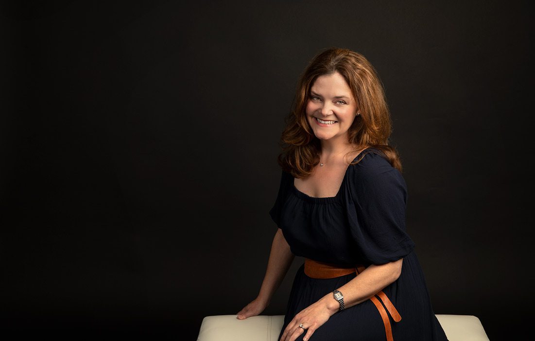 Lucie Amberg sits on white bench with black background