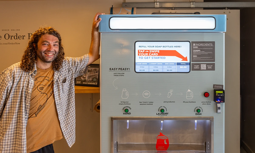 Adam McKay beside SOAP Refill Station's self-serve soap refill kiosk.