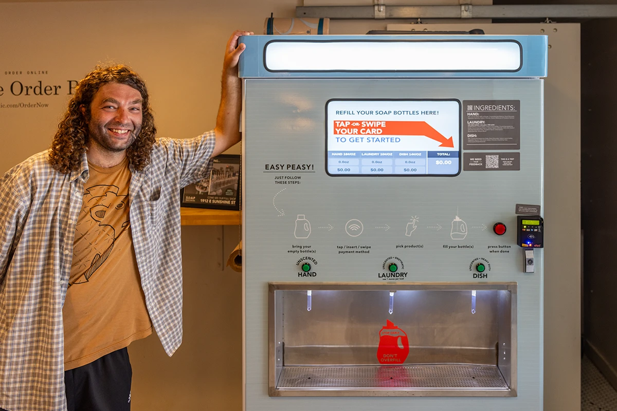Adam McKay beside SOAP Refill Station's self-serve soap refill kiosk.