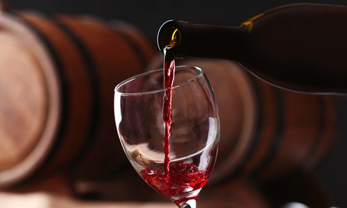 Red wine is poured into a glass against a background of stacked barrels.