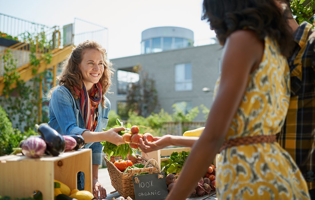 One woman hands produce to another woman at a farmers market