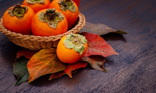 Persimmons on a table with fall-colored leaves.